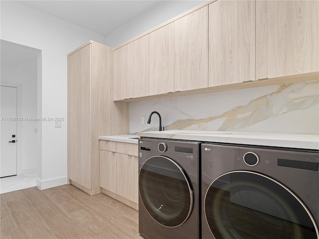 laundry area featuring washing machine and dryer, cabinet space, light wood-style floors, and a sink