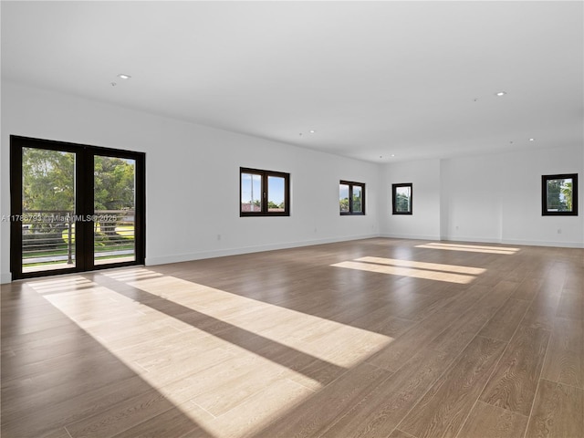 unfurnished living room with recessed lighting, wood finished floors, a healthy amount of sunlight, and baseboards