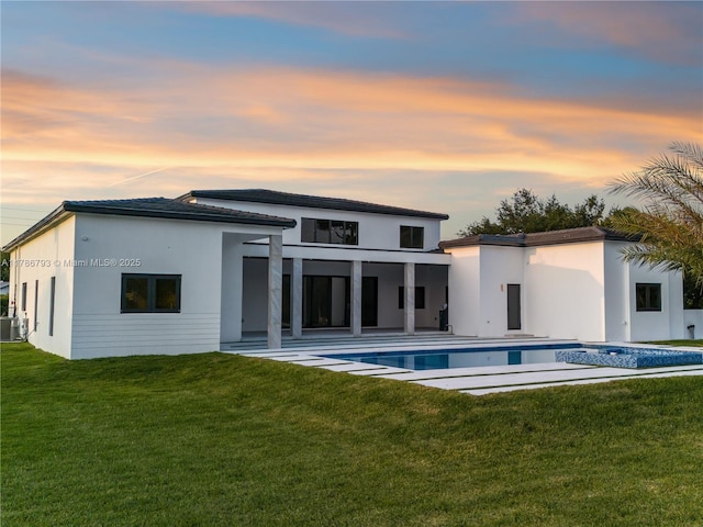 rear view of property with a lawn, an outdoor pool, a patio area, and stucco siding