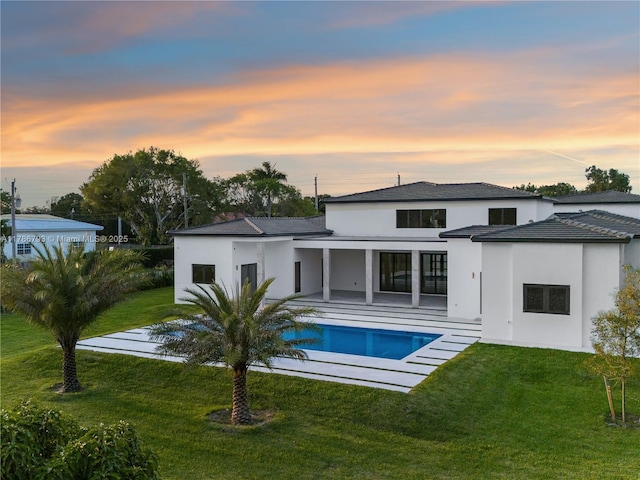 back of property at dusk with a patio area, an outdoor pool, a yard, and stucco siding