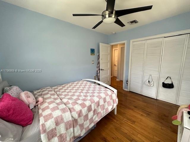 bedroom with a closet, wood finished floors, visible vents, and a ceiling fan