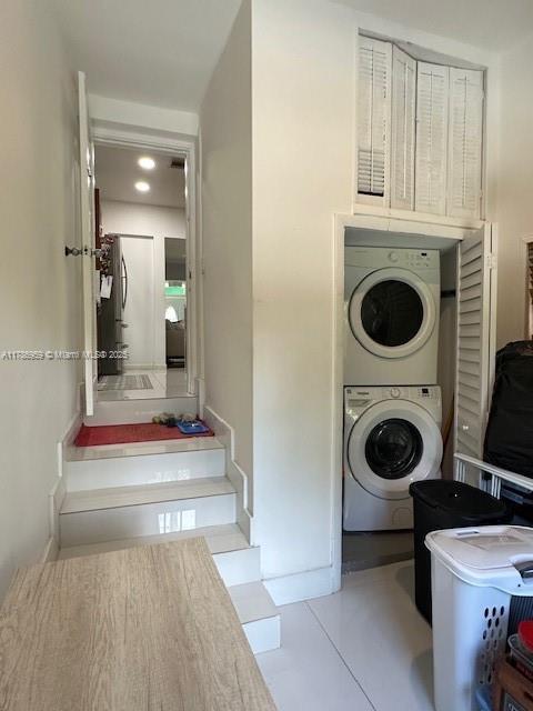 clothes washing area with stacked washer / drying machine, tile patterned floors, and laundry area