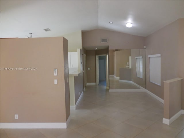 hallway featuring baseboards, visible vents, light tile patterned floors, and lofted ceiling