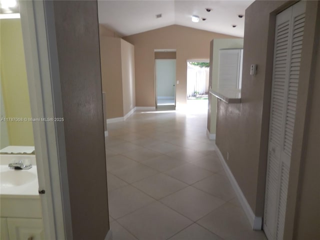 hall with baseboards, a sink, light tile patterned floors, and lofted ceiling