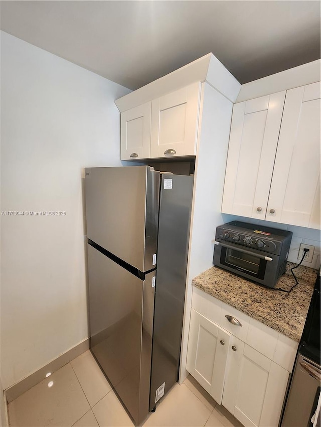 kitchen with white cabinetry, light stone countertops, light tile patterned flooring, and freestanding refrigerator