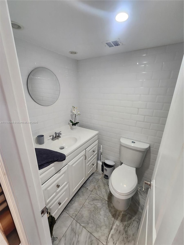 bathroom with vanity, tile walls, marble finish floor, toilet, and visible vents