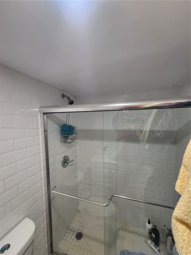 bathroom with a shower stall, toilet, and tile walls