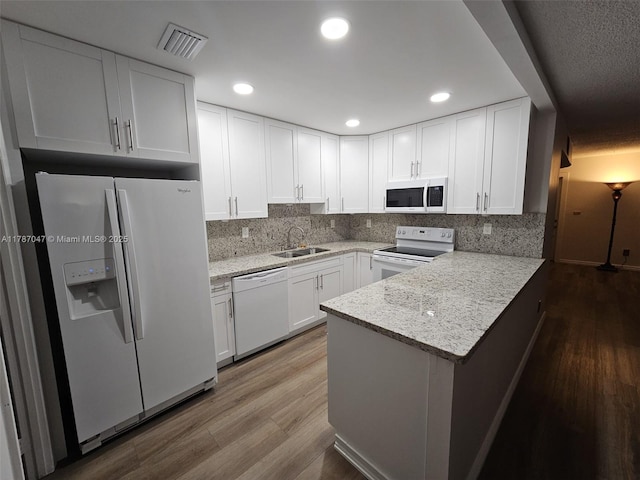 kitchen featuring visible vents, a sink, white appliances, a peninsula, and white cabinetry