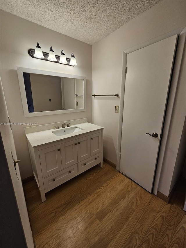 bathroom with baseboards, vanity, wood finished floors, and a textured ceiling