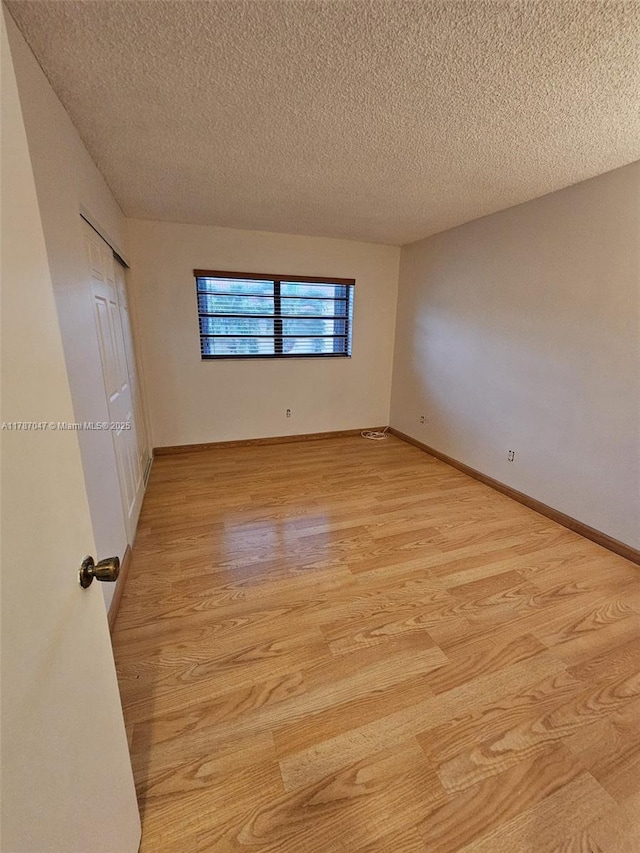 unfurnished bedroom featuring light wood-style flooring, a textured ceiling, and baseboards