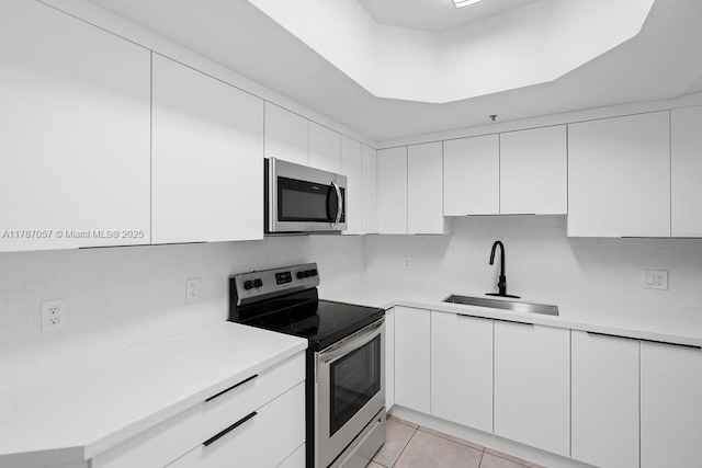 kitchen with stainless steel appliances, light countertops, a sink, light tile patterned flooring, and white cabinetry