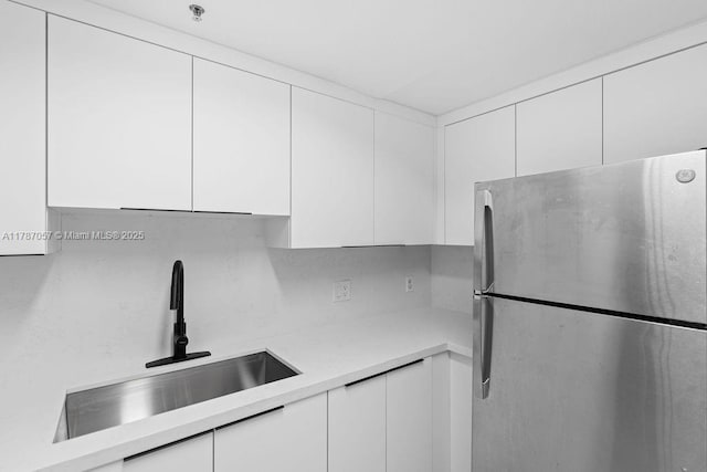 kitchen with a sink, modern cabinets, light countertops, white cabinetry, and freestanding refrigerator
