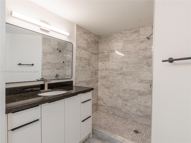 full bathroom featuring vanity, a textured ceiling, and tiled shower