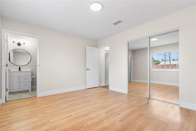 461 SE Evans Ave, Port St Lucie, FL 34984 - unfurnished bedroom featuring light wood finished floors, ensuite bath, a textured ceiling, baseboards, and a closet