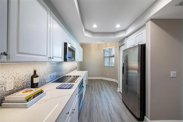 kitchen featuring stainless steel appliances, white cabinetry, light wood finished floors, baseboards, and decorative backsplash