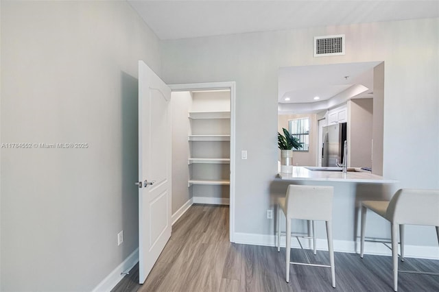kitchen with stainless steel fridge, wood finished floors, a kitchen breakfast bar, and white cabinetry