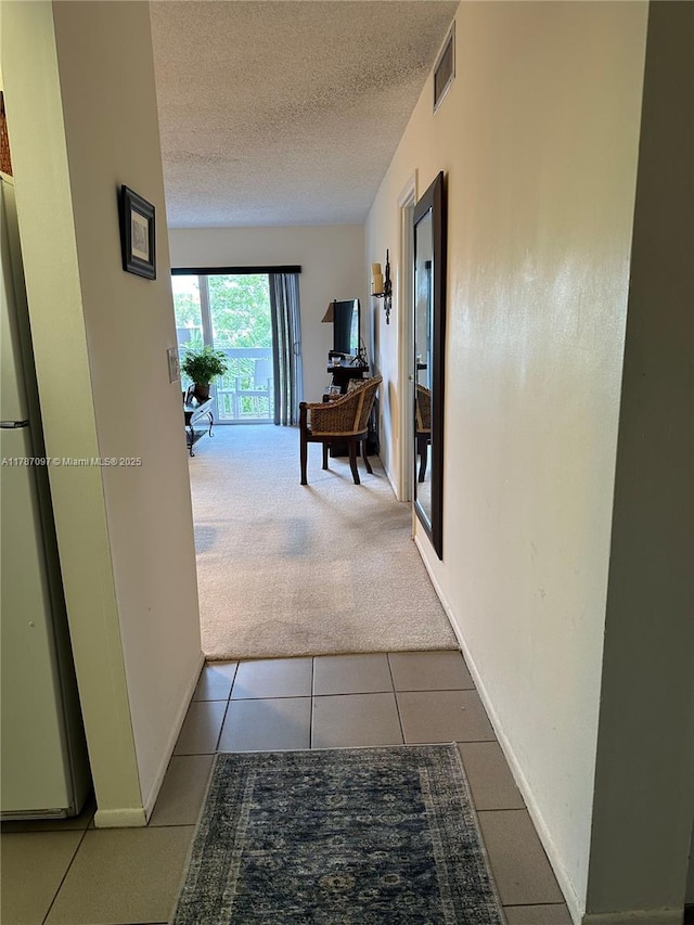 hallway featuring tile patterned floors, a textured ceiling, baseboards, carpet flooring, and visible vents
