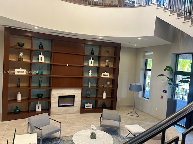 living area with a tiled fireplace, a high ceiling, baseboards, and light tile patterned floors