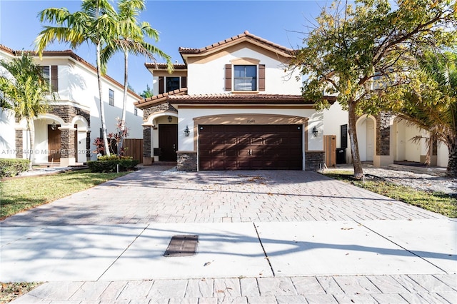 mediterranean / spanish-style house featuring a tiled roof, stone siding, an attached garage, stucco siding, and decorative driveway