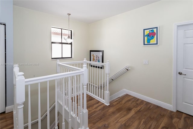 staircase featuring wood finished floors, baseboards, and a notable chandelier