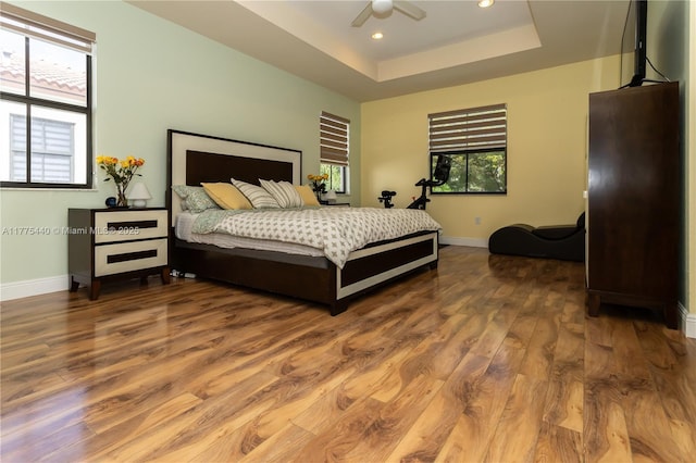 bedroom featuring a ceiling fan, wood finished floors, a tray ceiling, baseboards, and recessed lighting
