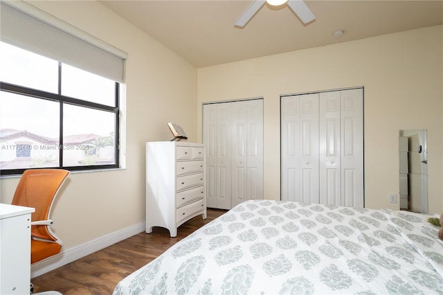 bedroom featuring a ceiling fan, baseboards, dark wood-type flooring, and two closets