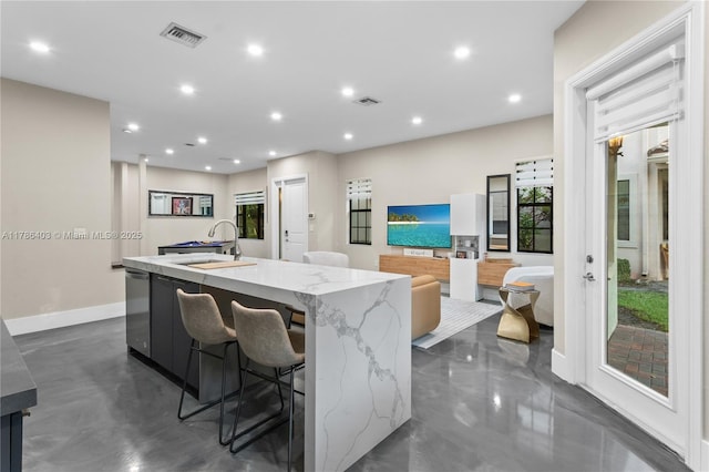 kitchen featuring visible vents, an island with sink, light stone counters, and a sink