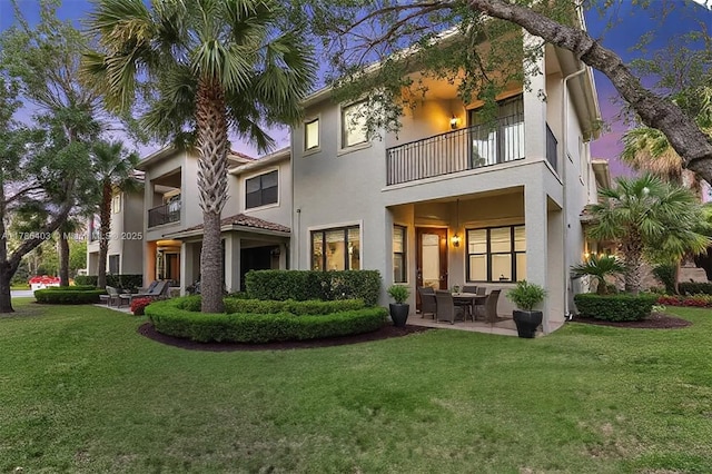 rear view of property featuring a lawn, a balcony, a patio area, and stucco siding