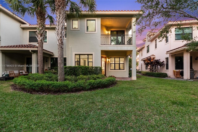 back of house featuring stucco siding, a tiled roof, a balcony, and a lawn