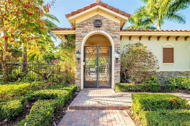 property entrance with a tile roof, stone siding, stucco siding, and fence