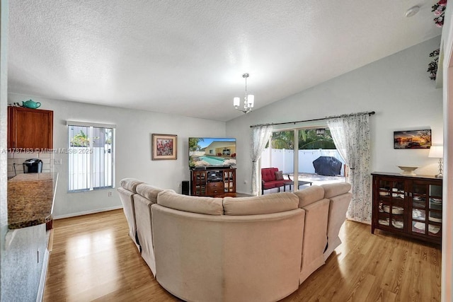 living area with light wood finished floors, a textured ceiling, baseboards, an inviting chandelier, and lofted ceiling