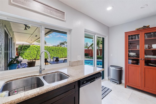 kitchen featuring stainless steel dishwasher, a sink, recessed lighting, light stone countertops, and light tile patterned floors