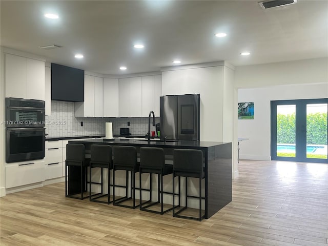 kitchen with dark countertops, smart refrigerator, tasteful backsplash, light wood-type flooring, and a breakfast bar