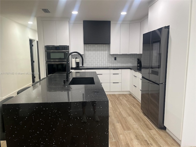 kitchen featuring decorative backsplash, white cabinets, freestanding refrigerator, double oven, and light wood-style floors