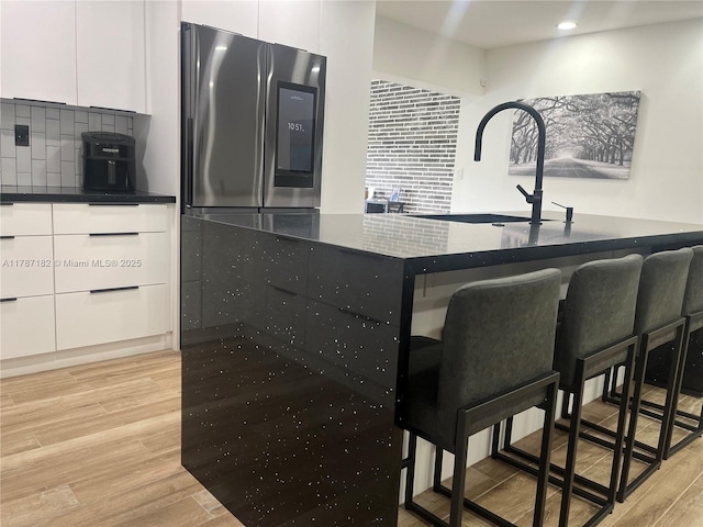 kitchen featuring decorative backsplash, a breakfast bar area, smart refrigerator, white cabinetry, and light wood-style flooring