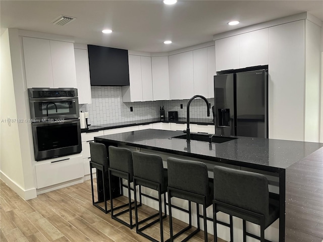 kitchen with visible vents, a sink, stainless steel fridge with ice dispenser, multiple ovens, and a breakfast bar