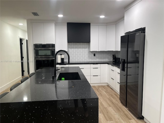 kitchen featuring double wall oven, visible vents, modern cabinets, light wood-type flooring, and black fridge
