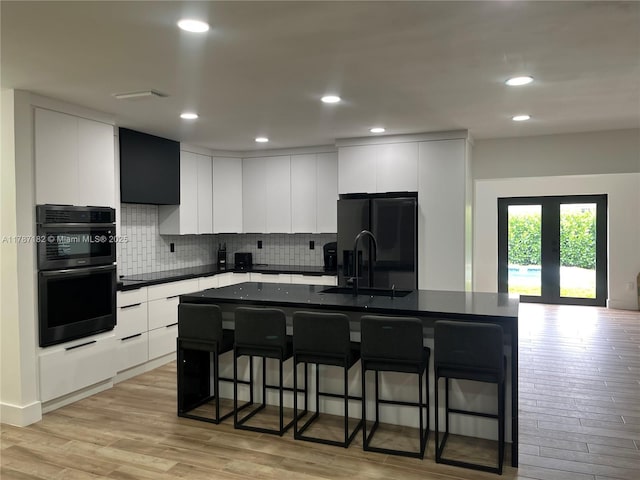 kitchen with a kitchen bar, dark countertops, a sink, white cabinets, and black appliances