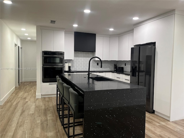 kitchen featuring a kitchen breakfast bar, tasteful backsplash, a sink, light wood-style flooring, and black appliances