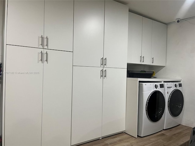 laundry area with cabinet space, separate washer and dryer, and light wood-style floors