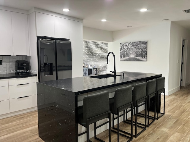 kitchen featuring black fridge with ice dispenser, a breakfast bar area, white cabinets, a sink, and light wood-style flooring