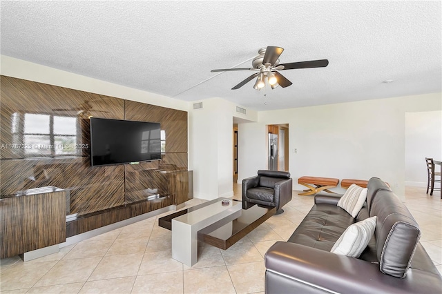 living room with ceiling fan, a textured ceiling, visible vents, and light tile patterned floors