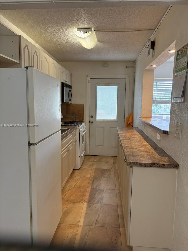 20311 NE 2nd Ave Unit 27, Miami, FL 33179 - kitchen with white appliances, plenty of natural light, dark countertops, a textured ceiling, and light stone finish floors