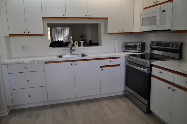 kitchen featuring white microwave, light countertops, stainless steel electric stove, a sink, and light wood-style flooring