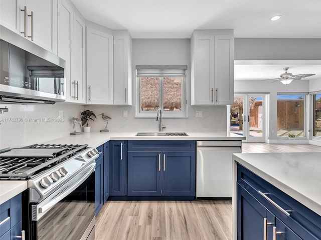 kitchen with blue cabinets, stainless steel appliances, a sink, and light wood-style floors