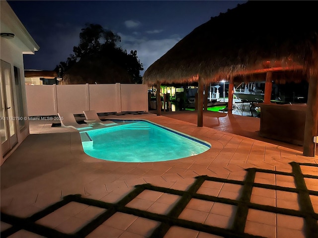 pool at night with fence, a patio area, and a fenced in pool