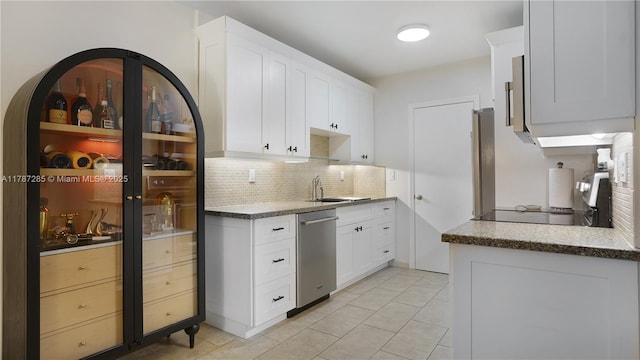 kitchen featuring white cabinets, stainless steel dishwasher, a sink, light tile patterned floors, and decorative backsplash