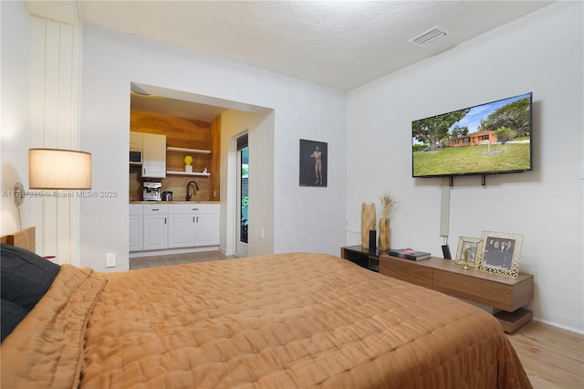 bedroom featuring light wood finished floors, visible vents, a sink, baseboards, and ensuite bathroom
