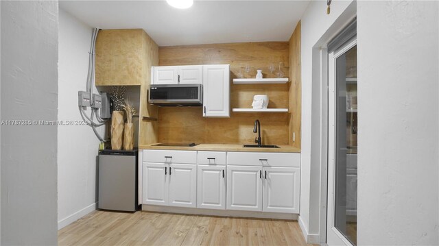 kitchen featuring light wood finished floors, a sink, stainless steel microwave, and white cabinetry