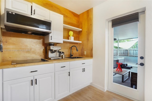 kitchen featuring black electric cooktop, a sink, stainless steel microwave, decorative backsplash, and light wood-style flooring